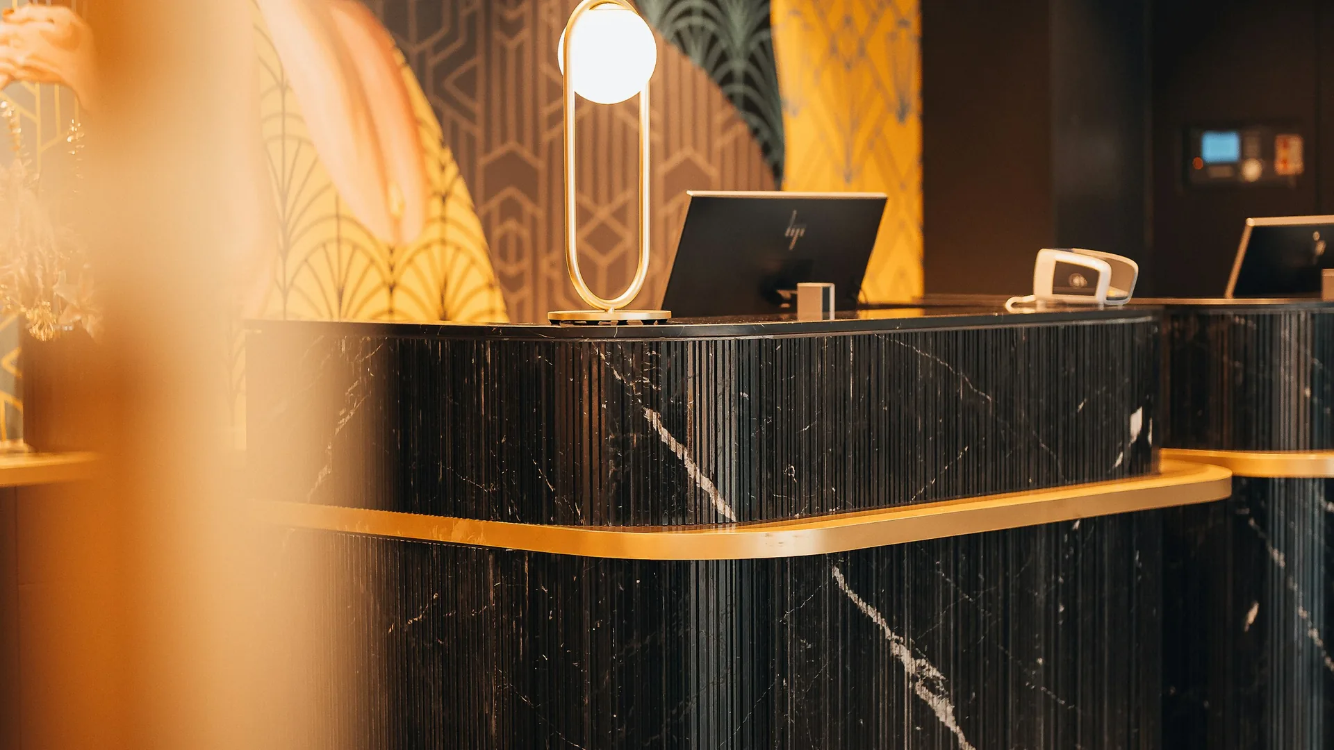 A hotel reception desk in black marble and brass, lit and empty.